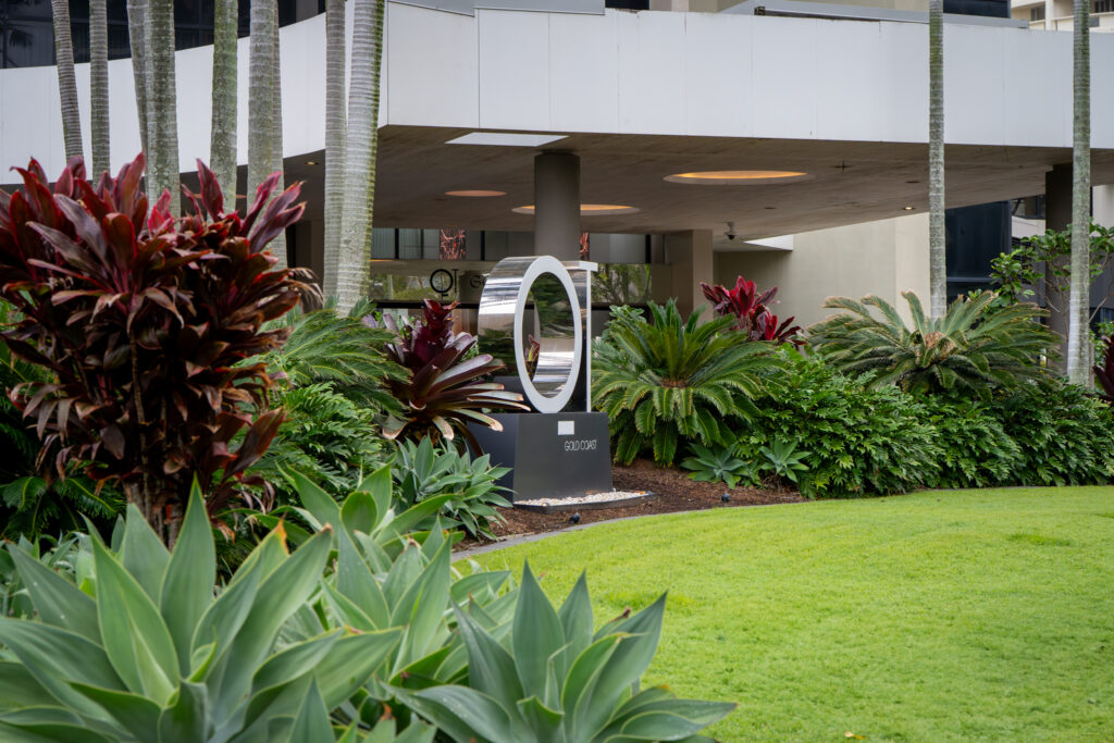Lawn with agaves, red cordylines and a ring sculpture beneath the hotel porte cochère at QT Gold Coast, Surfers Paradise